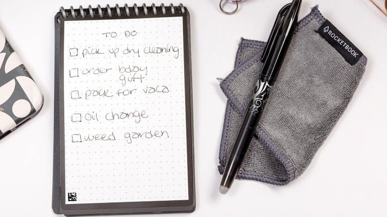 A Rocketbook New Mini with a to-do list written in it, besides a pen and cleaner.