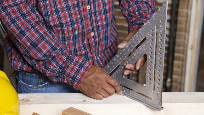 Man measuring straight line on wood using triangle square