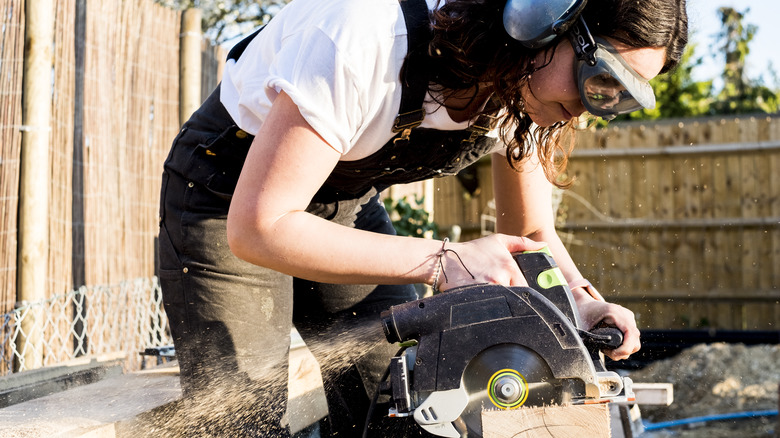 Woman bending over while sawing wood outdoors