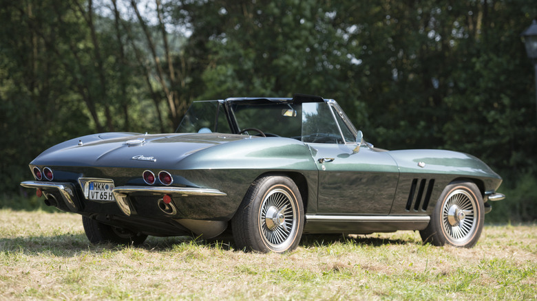 A steel blue C2 Corvette Sting Ray coupe rolling down a tree-lined road.
