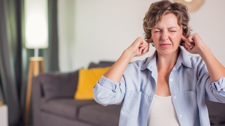 Person in their living room blocking their ears from loud noise