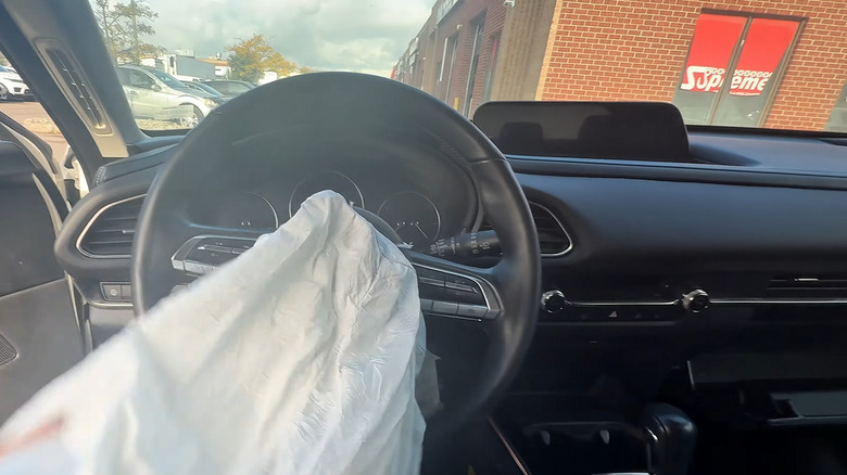 A technician holding the deployed steering wheel airbag in a Mazda CX-30.