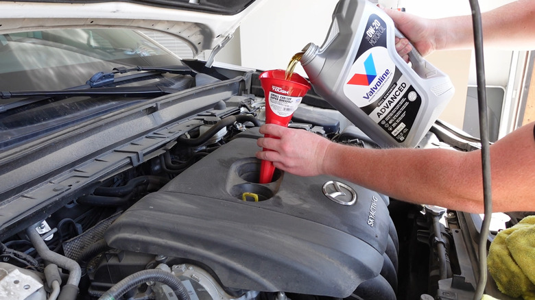 A man filling Valvoline 0W-20 motor oil into a SkyActiv-G 2.5-liter engine in a Mazda CX-30.
