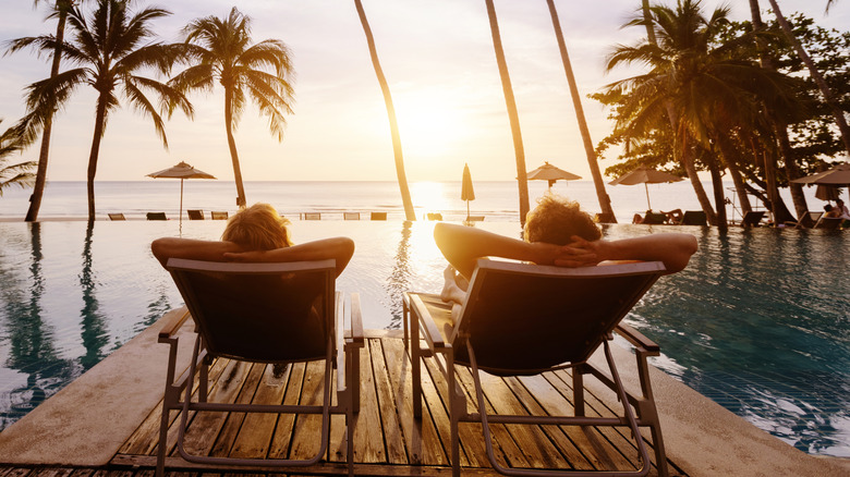 a couple sitting in lawn chairs are watching the sunset next to a resort swimming pool