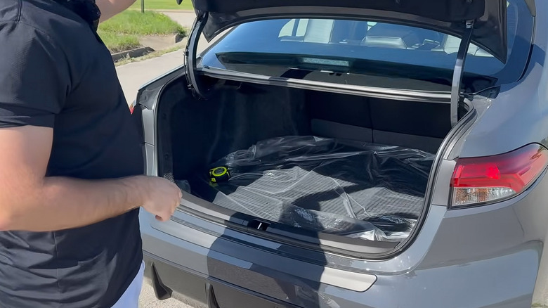 A man standing next to the open rear tailgate of a 2026 Toyota Corolla, showing the empty cargo area.
