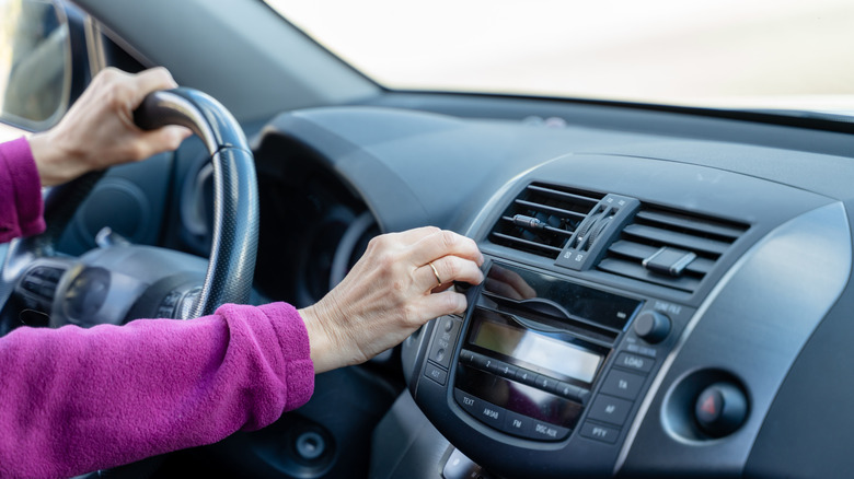 A driver in a purple shirt adjusting the volume for the stereo of an older, mid-2010 era vehicle.