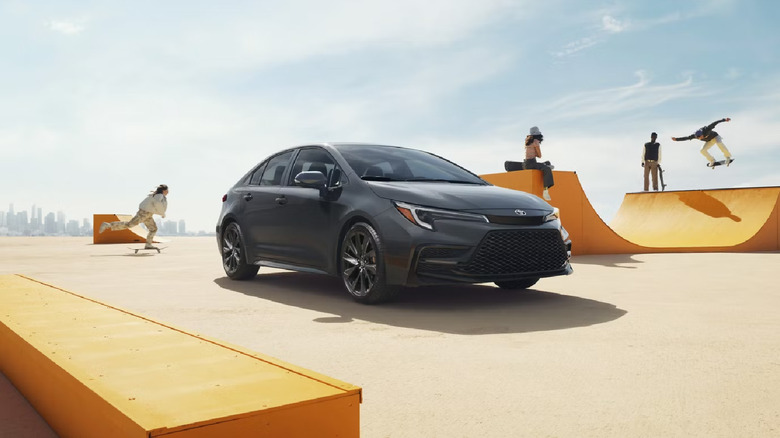 A gray 2026 Toyota Corolla compact car standing in a neo-urban skate park, with skaters in the backdrop.