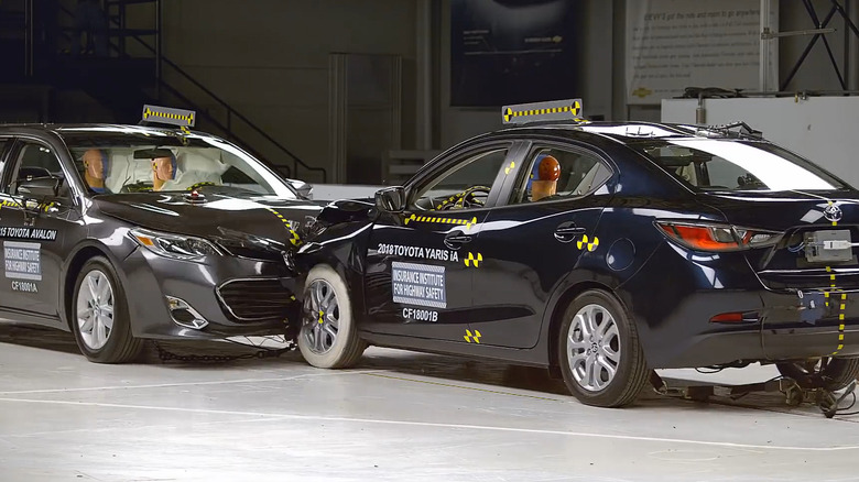 A black 2018 Toyota Yaris compact car being used in a front-on collision test with a black 2018 Toyota Avalon by the IIHS.