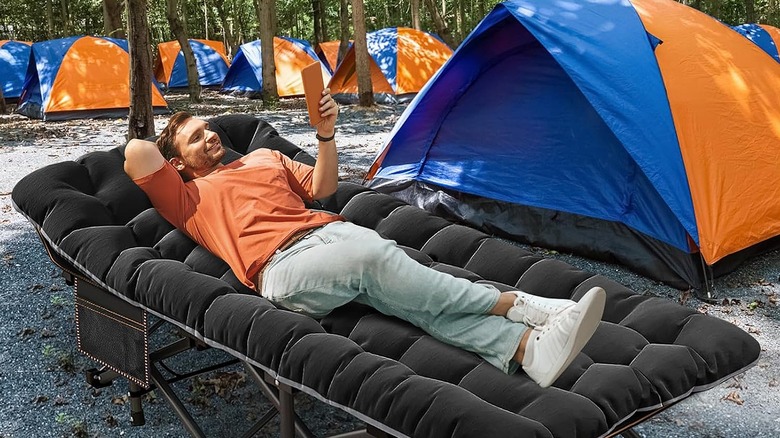 Man using a smartphone while lying in a camping cot at a campsite.