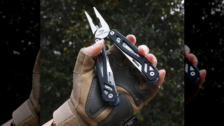 Man holding a multitool in front of a blurred tree,