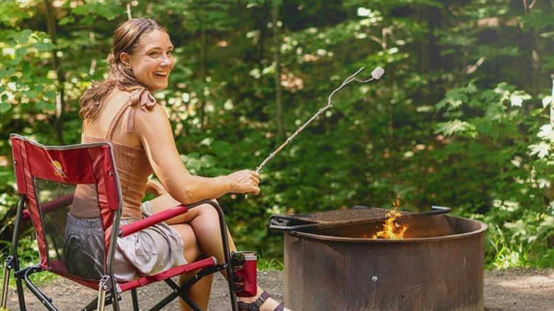 A woman sitting on the GCI Outdoor Freestyle Rocker roasting marshmallows on a campfire.