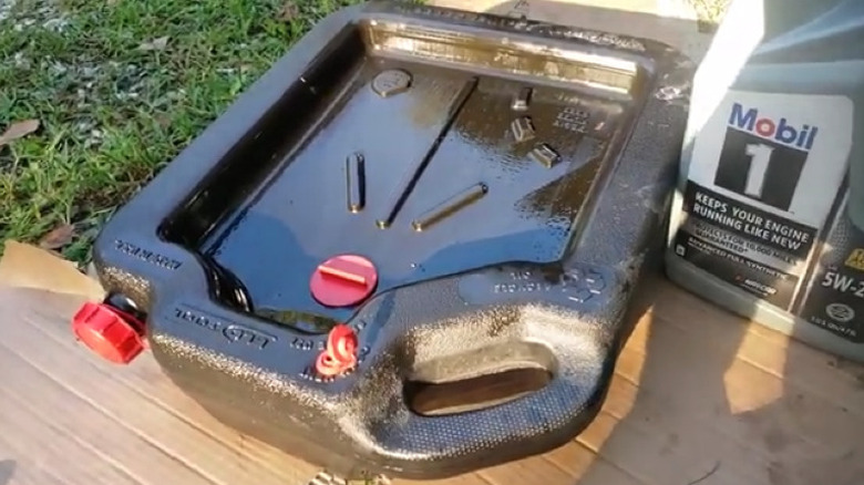 oil drain pan on grass and cardboard with motor oil bottle