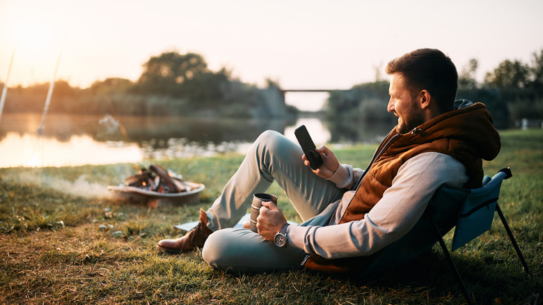 man using a phone by campfire