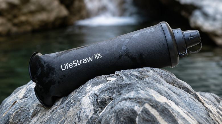 Portable water filter bottle laying on a rock by a river