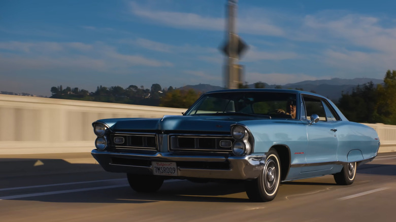 A metallic blue 1967 Pontiac Grand Prix, estimated to be from 1965, driving at speed down a highway.