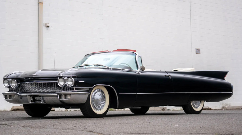 A 1960 Cadillac Series 62 in the convertible body style, finished in black, standing in front of an industrial building.