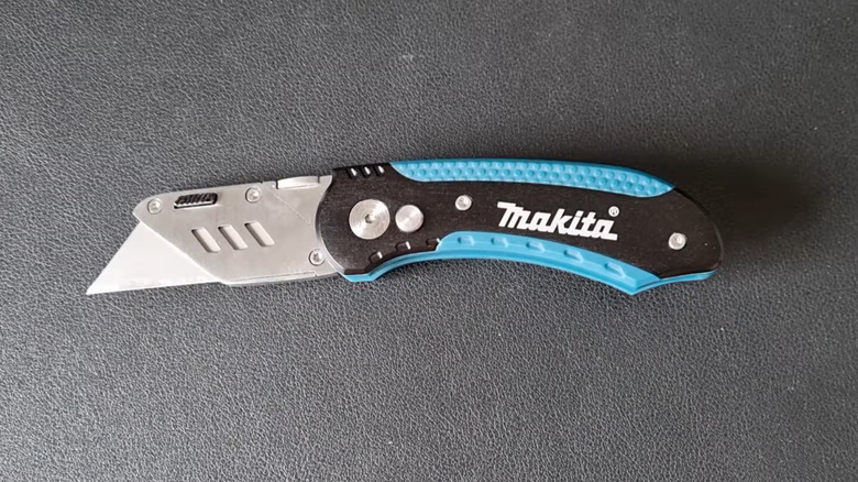 A Makita folding utility knife on a black surface.