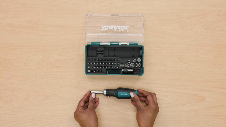 A person holds the Makita Ratchet in hand next to its bit set box.