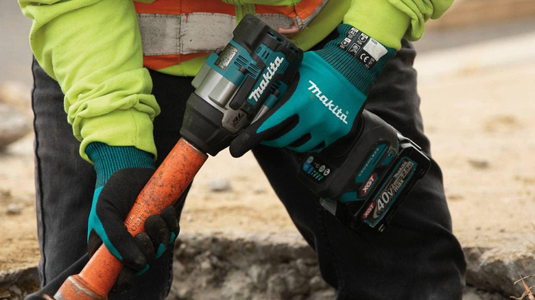 A person boring a hole in the ground while wearing work gloves.