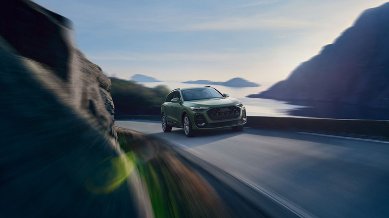 A dark green 2026 Audi Q5 SUV moving at speed down a hilly road with motion blur effects surrounding the car.