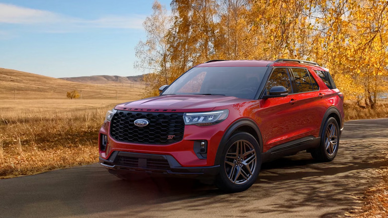 A red Ford Explorer ST standing on a dusty country road with trees and an open field in the background.
