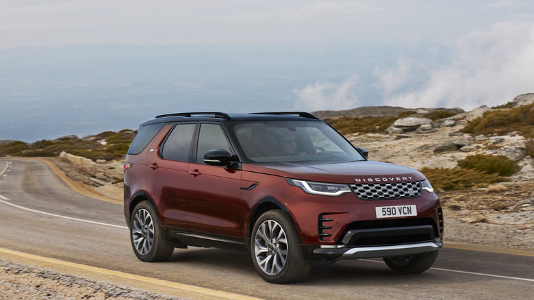 A satin red 2025 Land Rover Discovery, finished here in the "Tempest" special edition, moving along a rocky road.