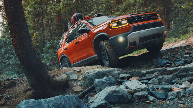 A 2026 Honda Passport pictured off-roading in a front-on view, finished here in Sunset Orange.