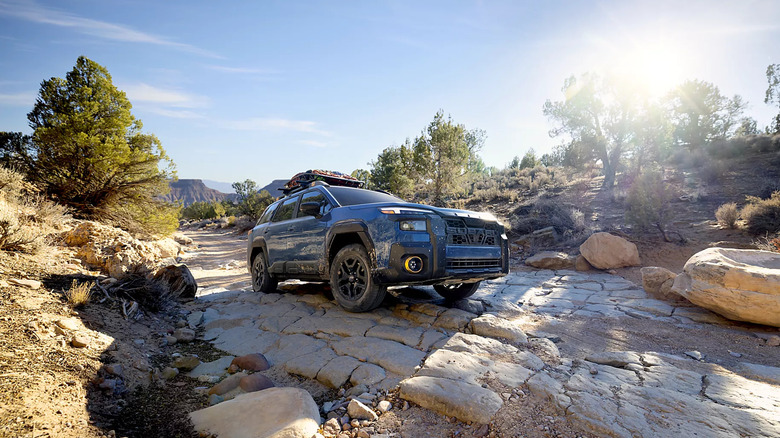 A dark blue 2026 Subaru Outback with cargo on the roof standing still on dry, cracked ground.