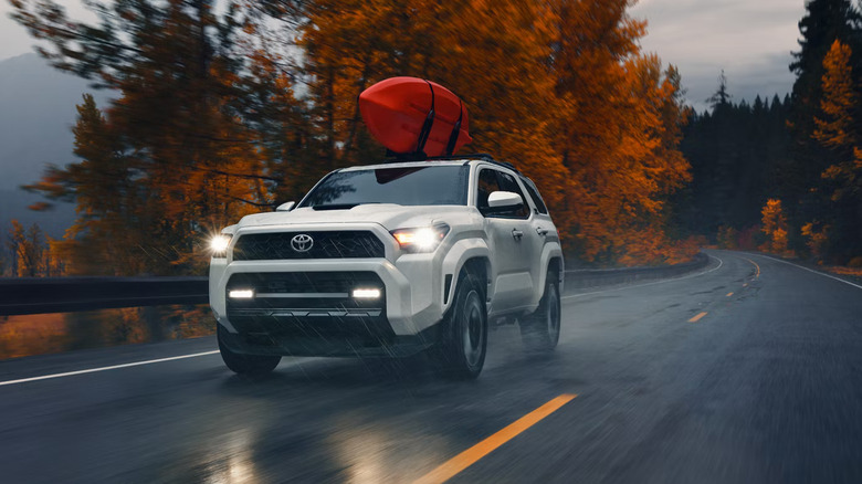 A white 2026 Toyota 4Runner SUV moving at speed down a road on a cloudy day with a kayak on the roof.