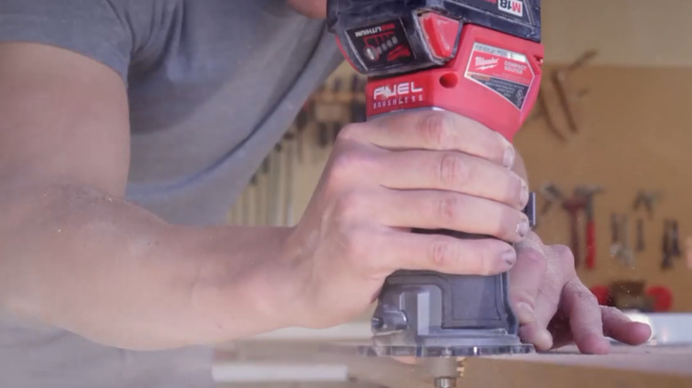 Milwakee M18 Compact Router cutting alongside of lumber piece