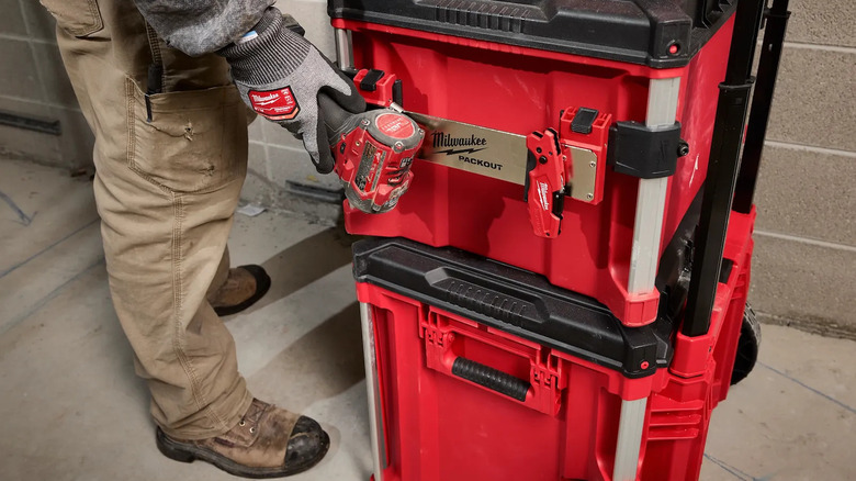 Person attaching a power drill to a stack of Packout boxes via a metal belt clip rack