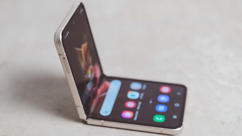A clamshell smartphone, propped up in a half-folded state on an off-white surface