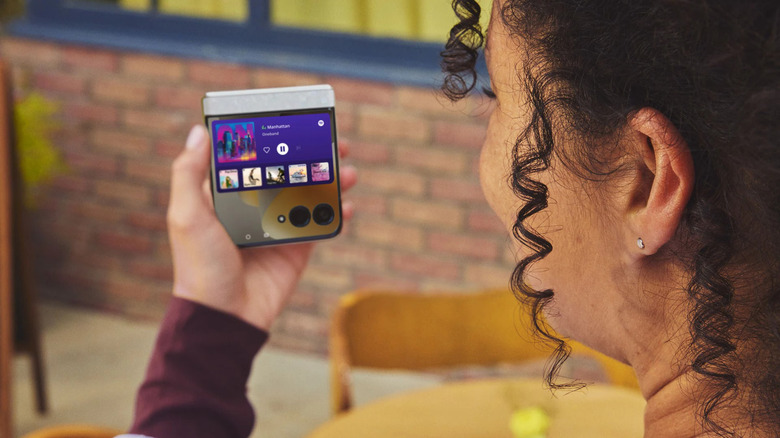 A person holding a folded 2026 Motorola Razr with music playing on it