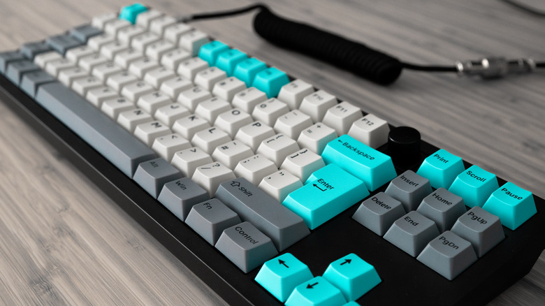 A black mechanical keyboard with white, gray, and cyan buttons on a wooden table