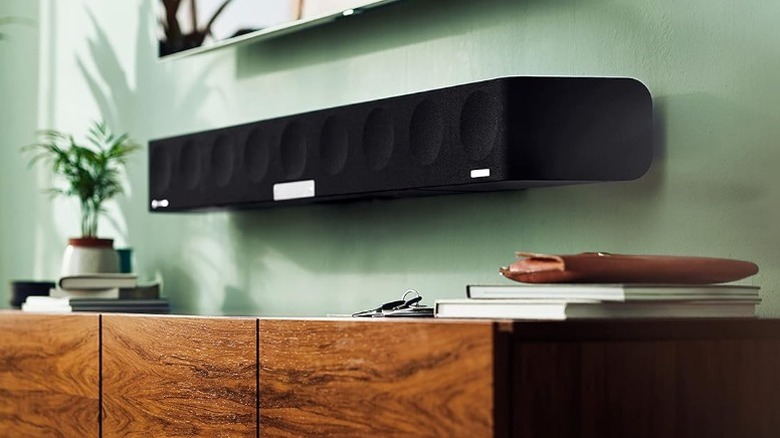 Sennheiser Ambeo Max soundbar wall-mounted on a green wall below a TV and above a wood cabinet