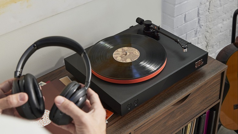 A person holding a set of headphones in front of a jbl spinner turntable