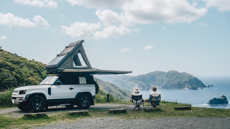 Rooftop tent open and couple looking out at water
