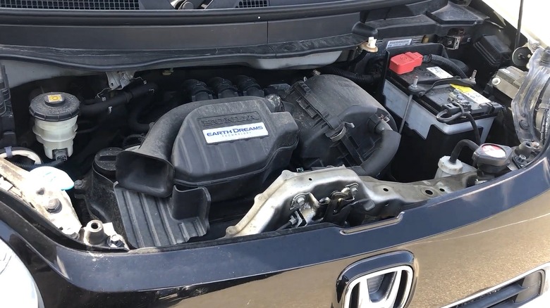 A Honda S07A engine bay wearing an Earth Dreams Technology cover badge, sitting inside what looks like a compact Japanese kei-style car with its propped opened hood.