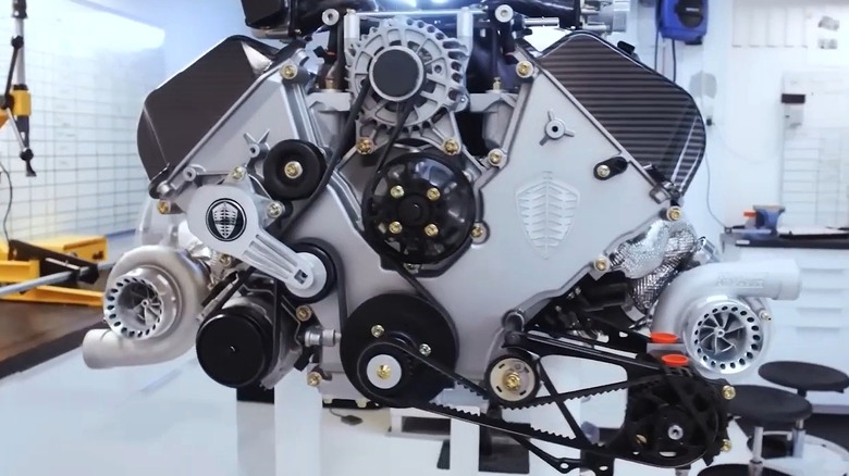 The Koenigsegg Tiny Friendly Giant rests on a display stand inside what looks like a pristine engineering lab, with its twin turbochargers mounted low on either side and the Koenigsegg logo stamped proudly in two places across the engine.