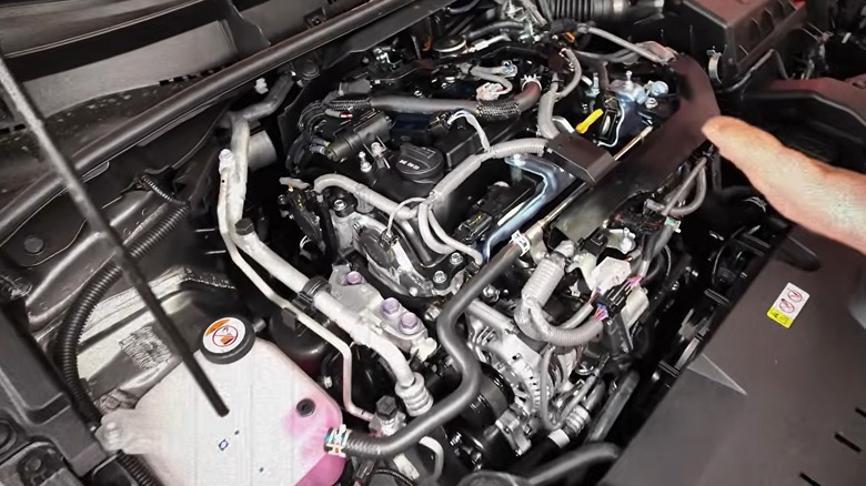 A densely packed Toyota G16E-GTS engine bay with an exposed three-cylinder unit surrounded by a web of hoses, wiring, and plumbing.