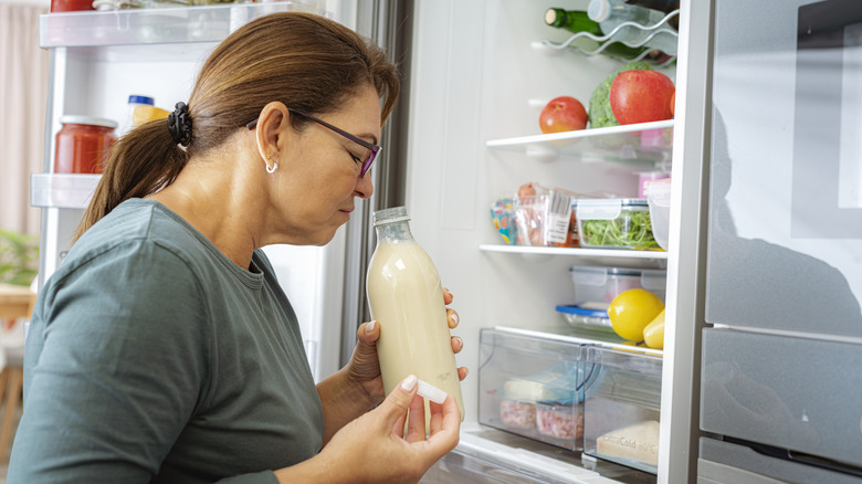 woman smelling spoiled milk in fridge