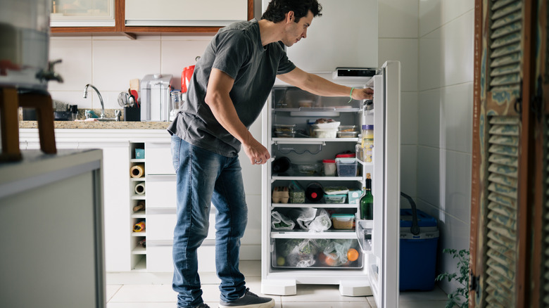 man looking in stuffed refrigerator