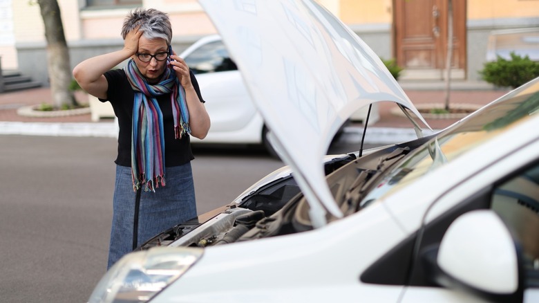 a person with car trouble standing in front of their car while on their cellphone