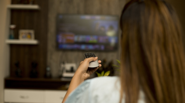 A person depicted from behind uses a remote on a TV