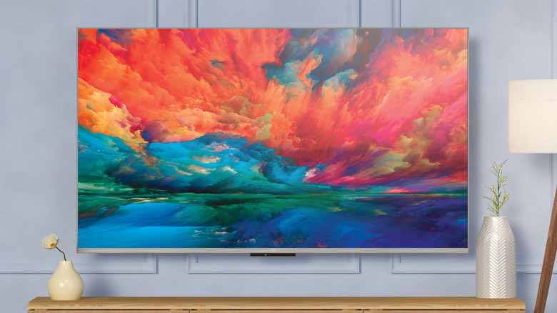 An Amazon Fire TV Omni QLED showing a colorful picture on a table in front of a gray wall