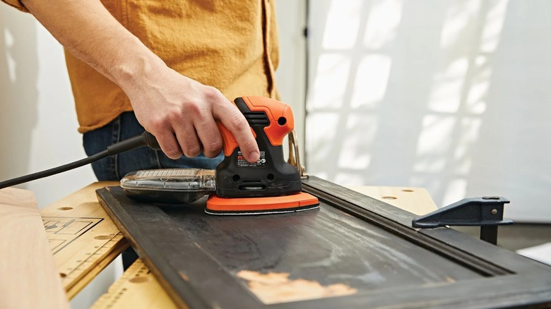 A person using a mouse sander on a wooden panel