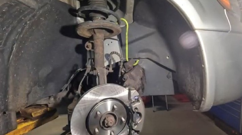 brake caliper hanging off strut above new brake rotor