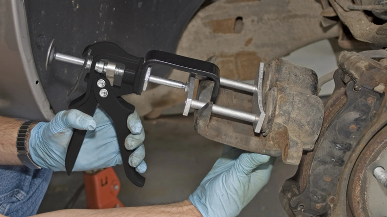 person using piston compressor on brake caliper