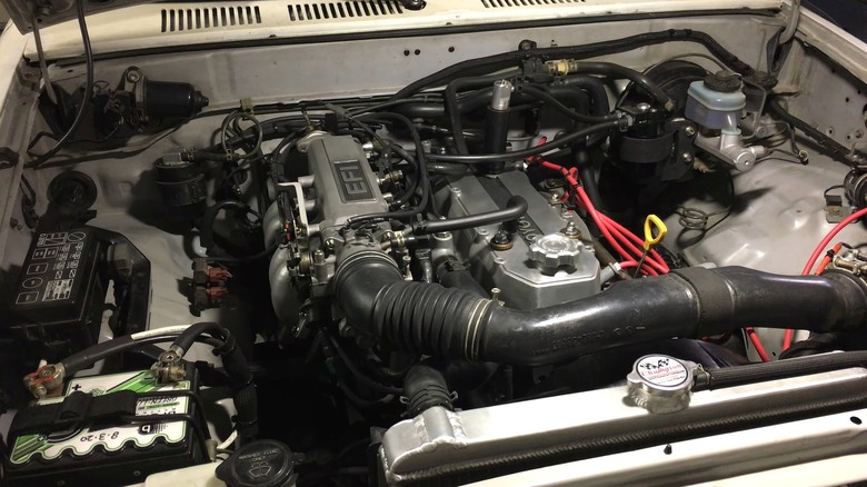 A clean Toyota 22R-E inline-four engine inside an older vehicle's engine bay, with visible intake tubing, wiring, and a compact mechanical layout.