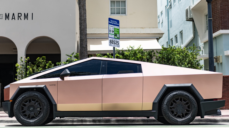 Pink Cybertruck in profile in front of shops